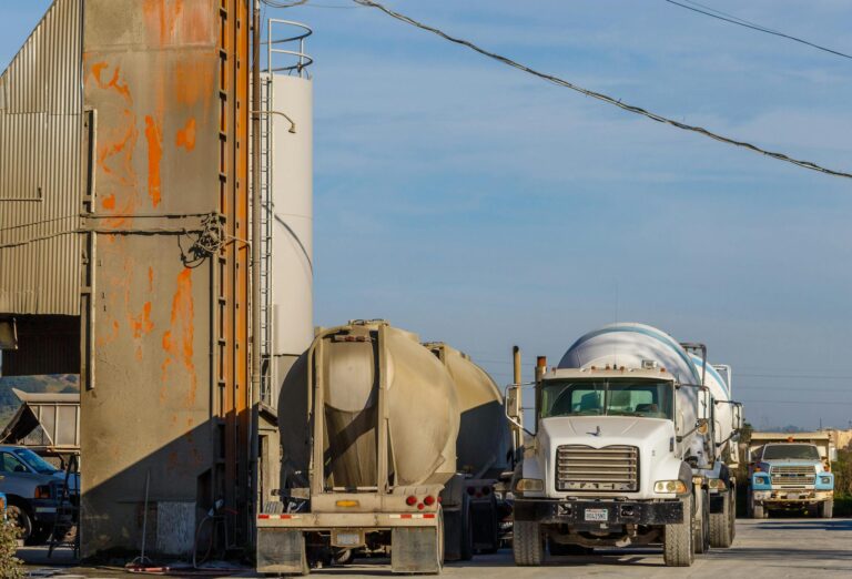 Heavy industrial trucks and tankers parked at a concrete production facility outdoors.