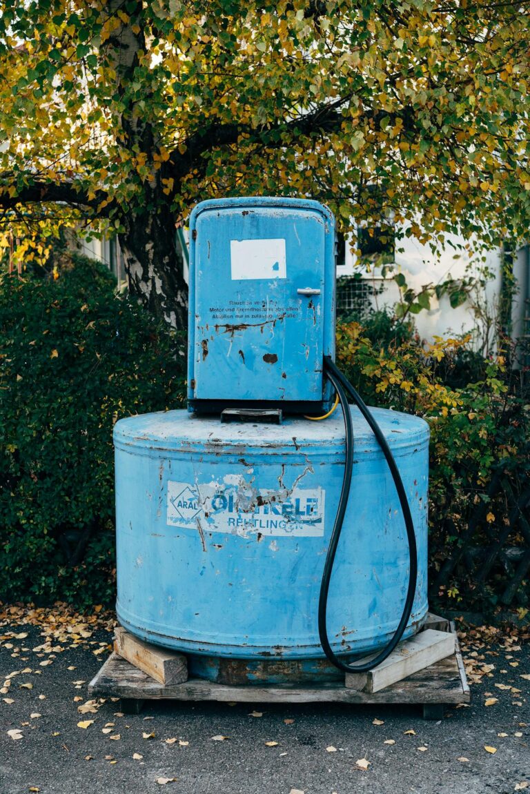 Old rusty blue oil tank in an outdoor setting with autumn foliage. Industrial equipment amidst natural scenery.